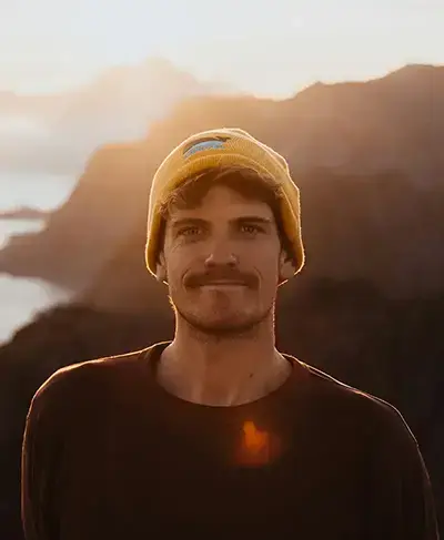 Ein junger Mann mit Bart und gelber Mütze schaut in die Kamera