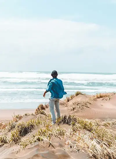 Ein junger Mann steht auf einer Düne im Wind und blickt auf das offene Meer