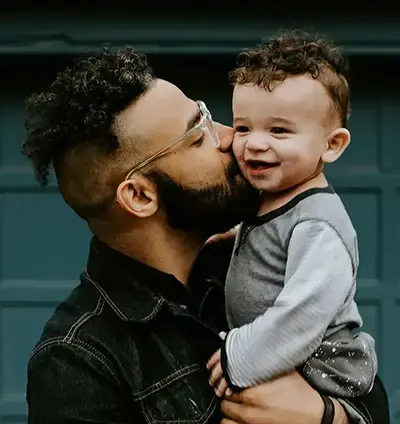Ein Vater hält seinen jungen Sohn in den Armen und gibt ihm einen Kuss auf die Backe