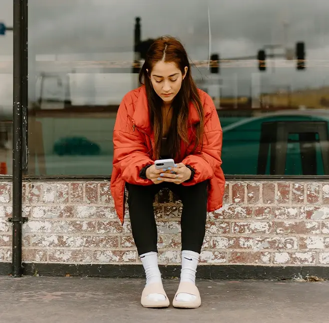 Eine Frau sitz an einem Fenster und benutzt ein Smartphone